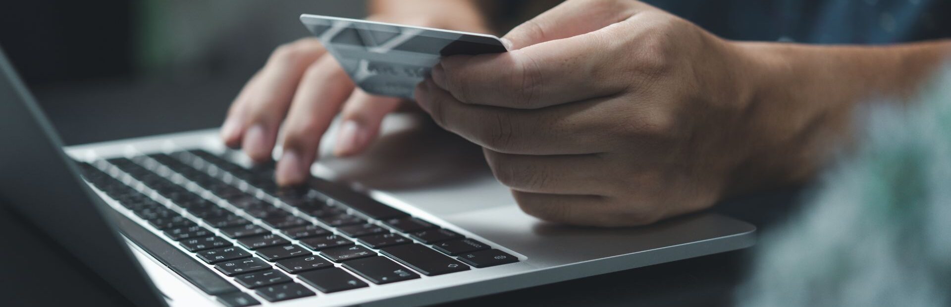 Mokėjimo kortelė rankoje ir nešiojamasis kompiuteris, atliekamas mokėjimas internetu